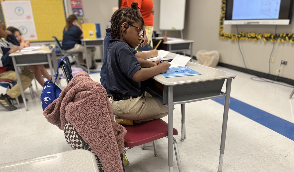 A girl in the foreground writes on a whiteboard.