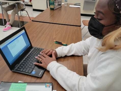 A student wearing a mask is working on a Chromebook.