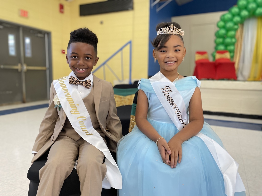 A child in a suit and a child in a dress, both wearing sashes.