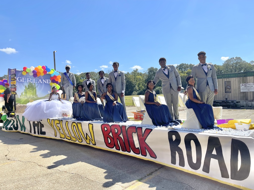 A group of 12 students are dressed up elegantly on a float that says "follow the yellow brick road."