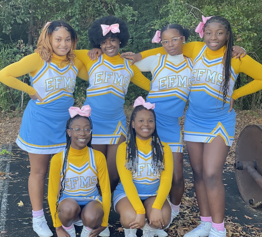 A group of 6 students wearing East Feliciana Middle School cheerleading uniforms in front of a verdant background.