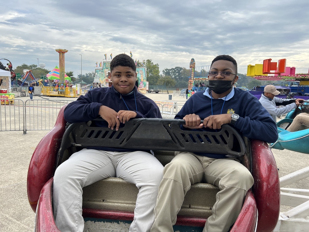 Two students sit on a fair ride. One is wearing a mask.