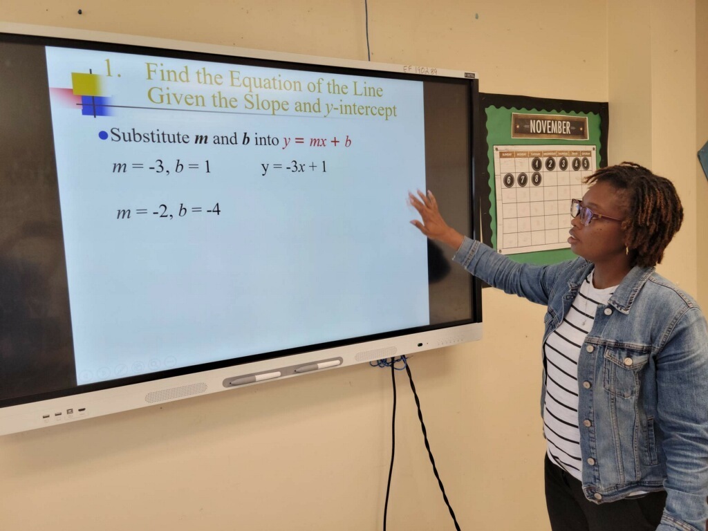 A teacher gestures towards a smartboard.
