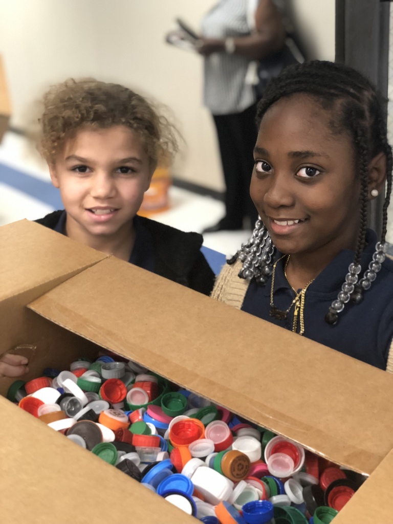 Two students hold a box of bottle caps.