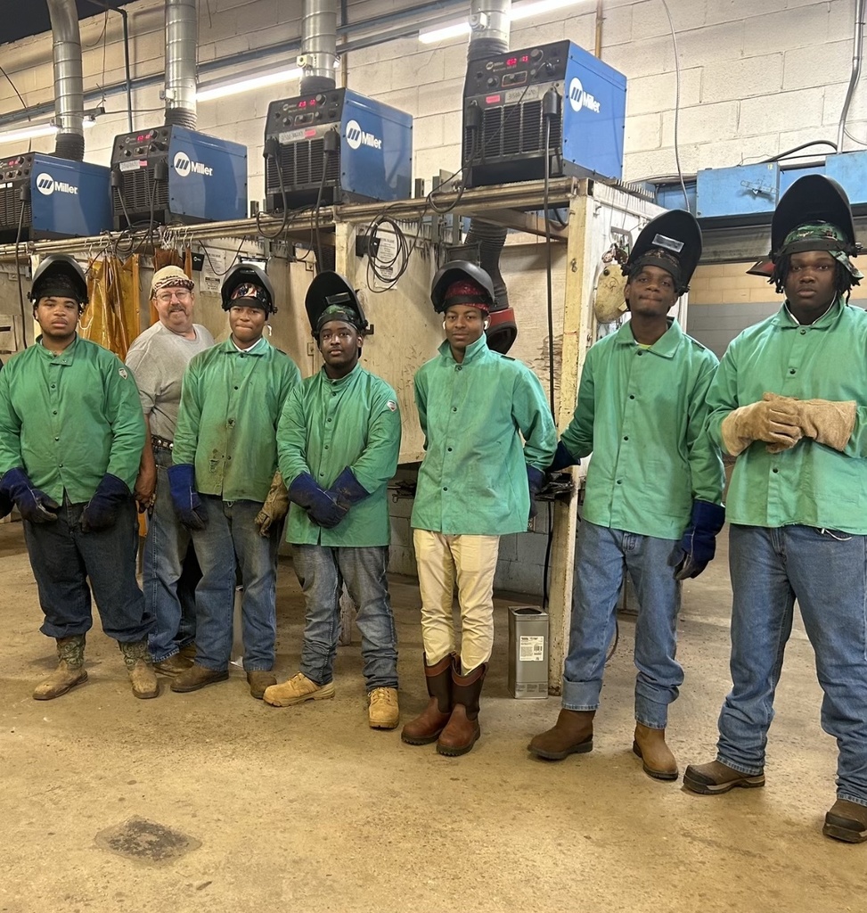 A group of students in welding hoods stand with an instructor.