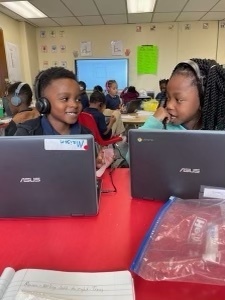 Two students at computers smile at each other.