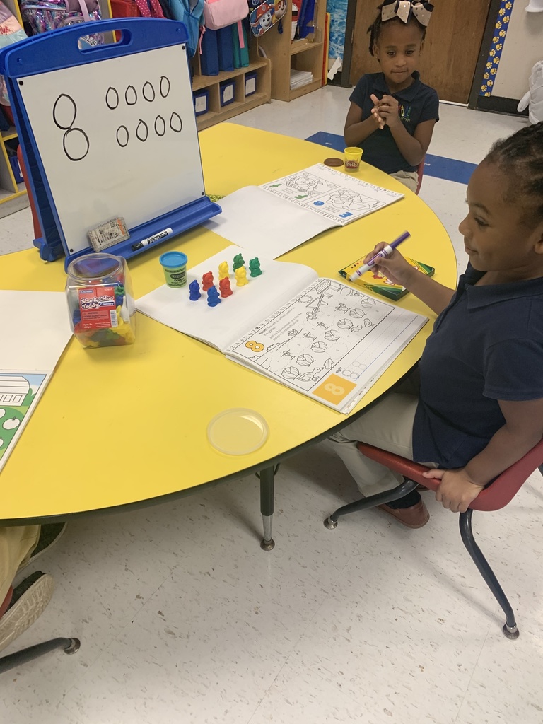 Two students make the number 8 while sitting at a bright yellow table.
