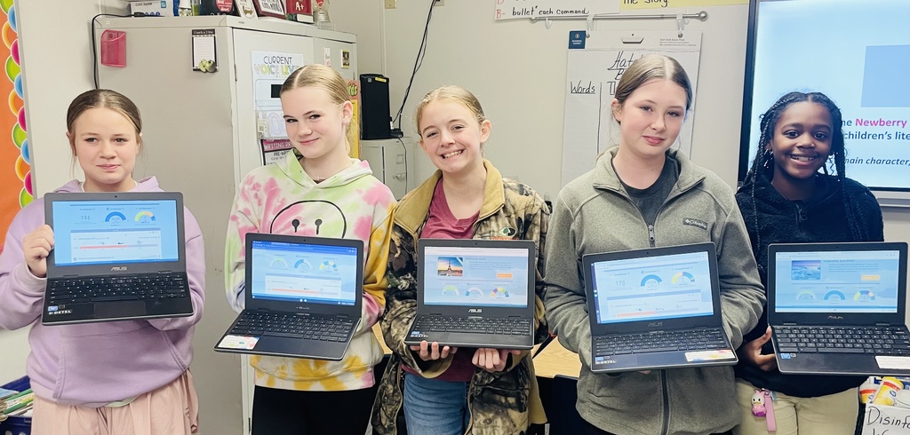 A group of smiling students holds up Chromebooks.