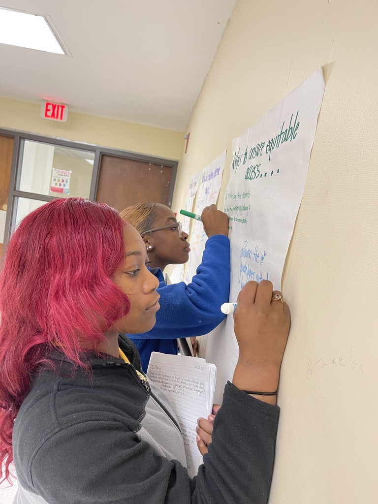 Two students are writing on chart paper that has the heading "Ways to ensure equitable access."