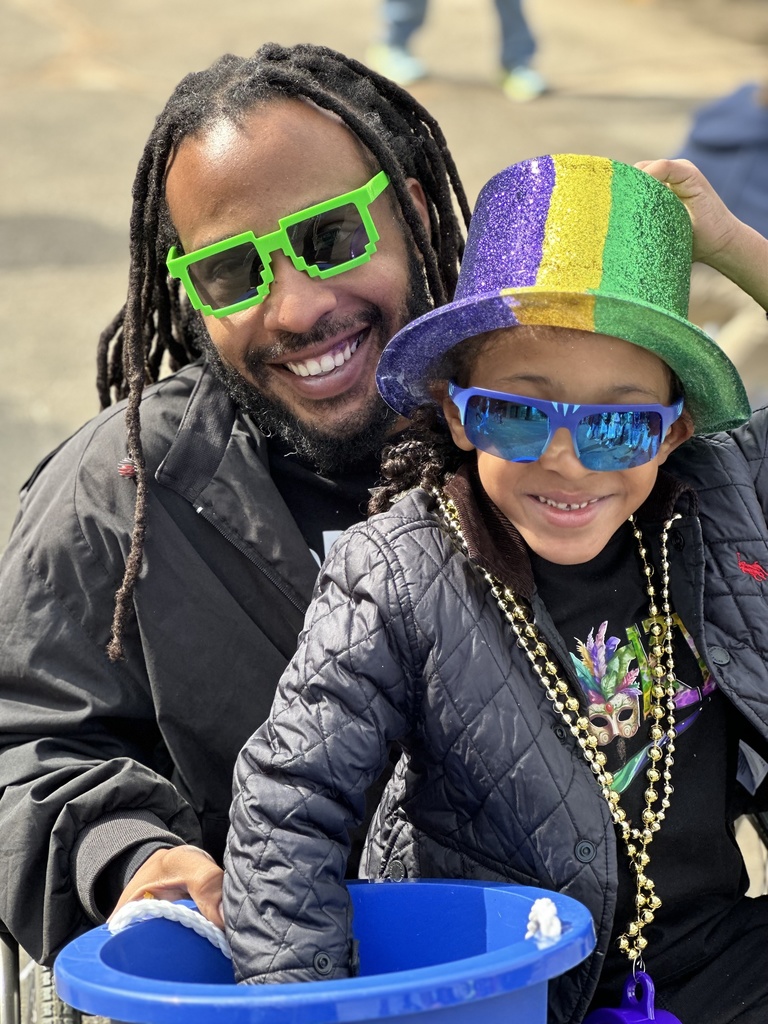 An adult and child are wearing cool sunglasses. The child is wearing a Mardi Gras hat.