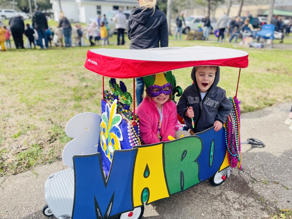 Two smiling children are in a wagon with a red topper with text on the side that says "MARDI."