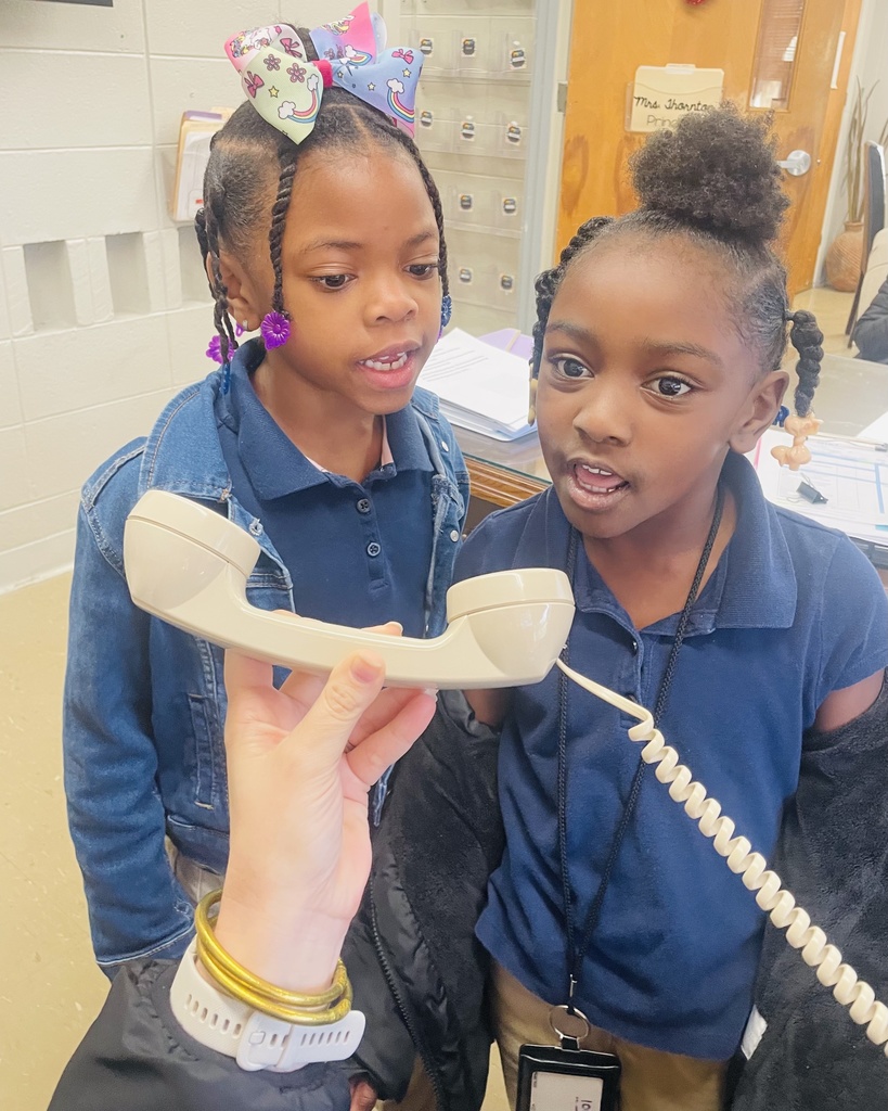 Two students lead the announcements over a telephone system in a school office.
