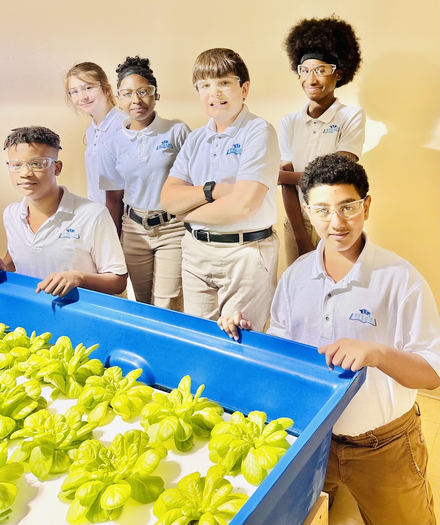 A group of six students stand and kneel behind a bed of lettuce in an aquaponics lab.