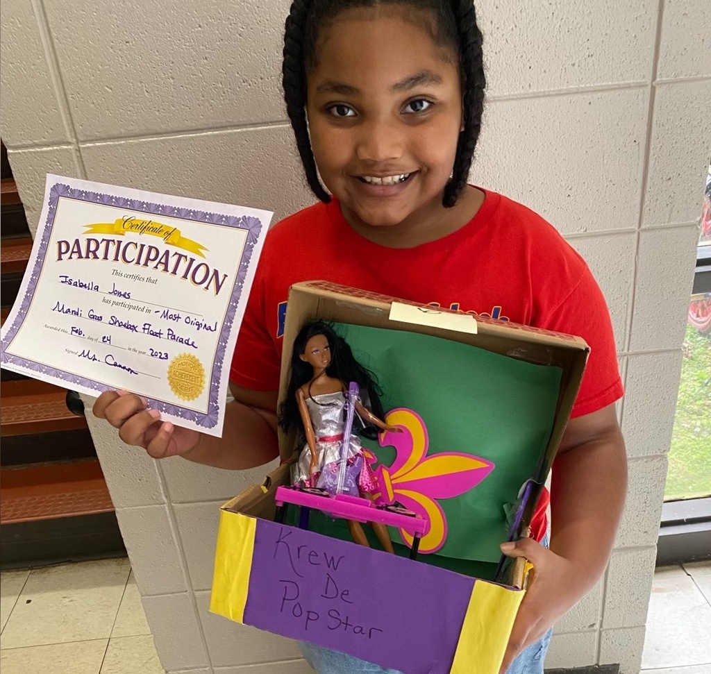 A student holds up a certificate and a shoebox display with a Barbie doll in it.