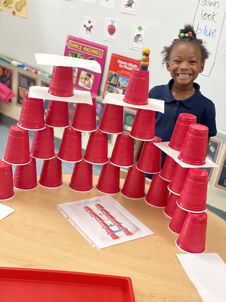 A child smiles standing by a collection of stacked red cups.