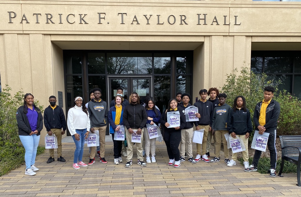  A group of people, mostly students, stand in front of a building labeled "Patrick F. Taylor Hall."