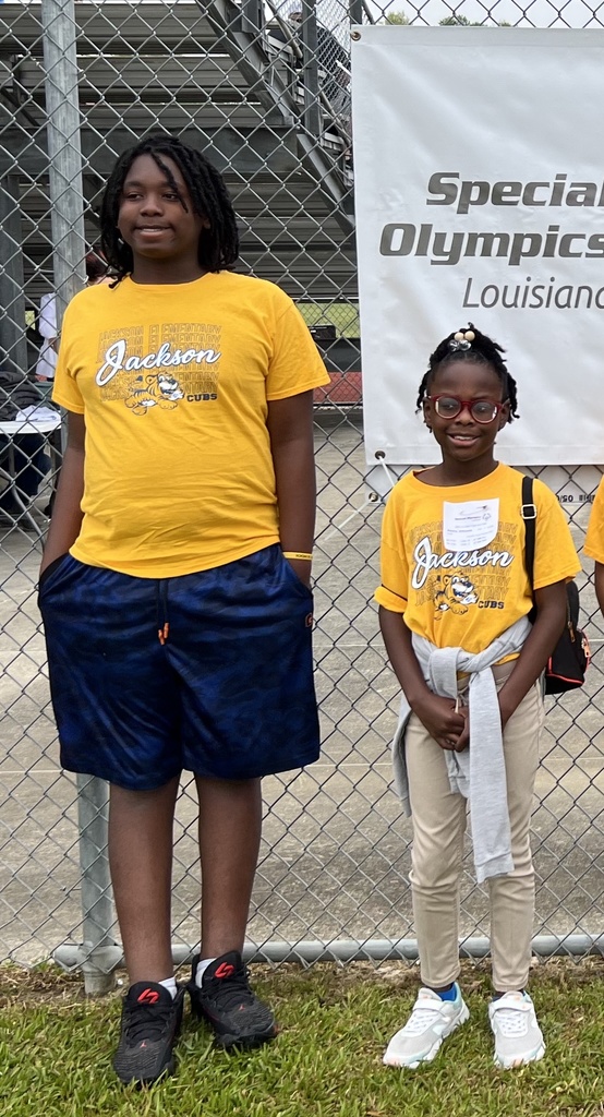 Two smiling children stand in front of a Special Olympics banner wearing gold shirts.