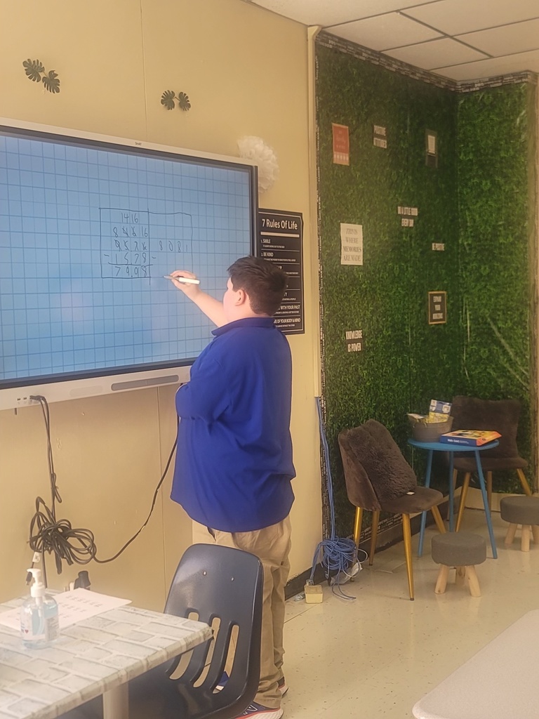 A student solves a math equation on a smartboard in a classroom.