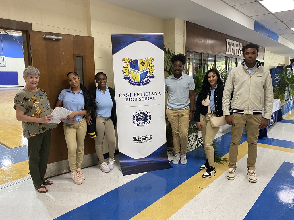 An adult and five high school students stand near an East Feliciana High School banner.