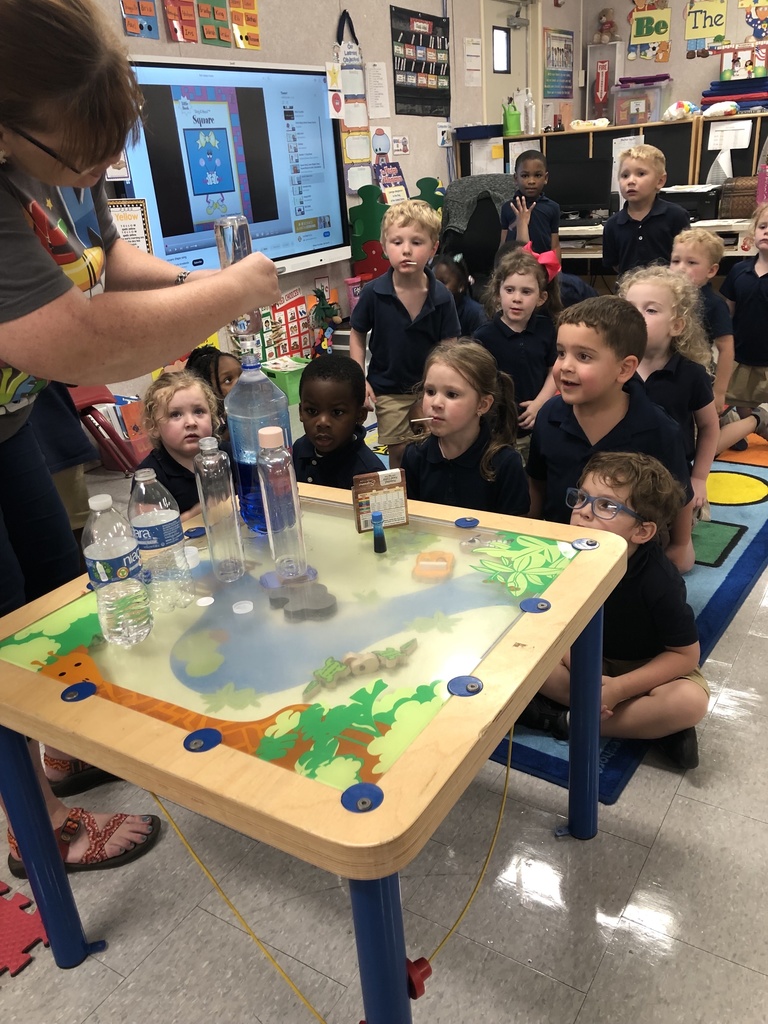 An adult does a science experiment as a group of children look on.